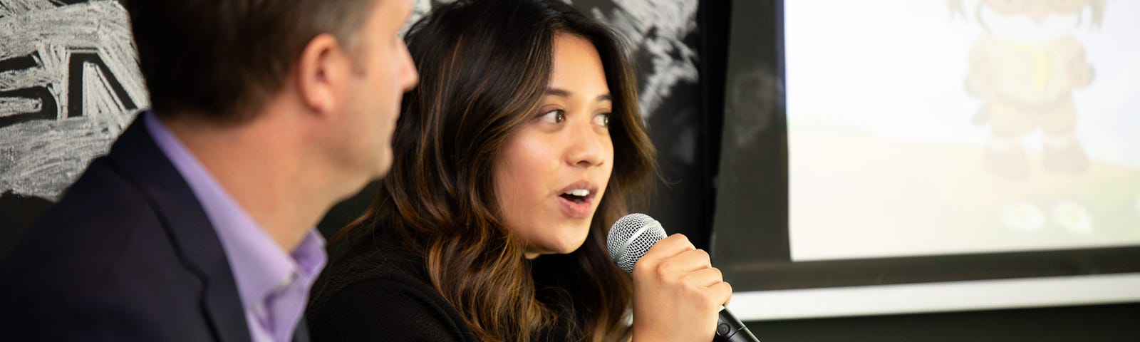 A woman with long, dark hair uses a microphone to speak at a Salesforce Partner event.