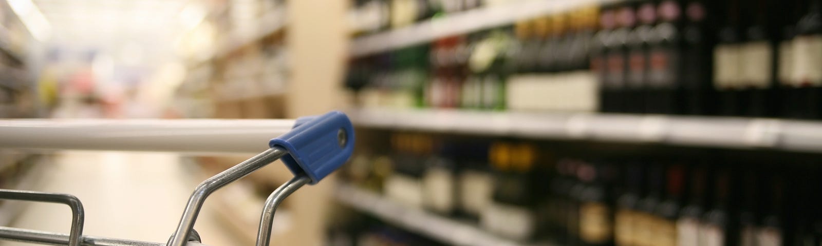 Close-up image of a shopping cart with a soft out-of-focus background of a wine aisle at a grocery store