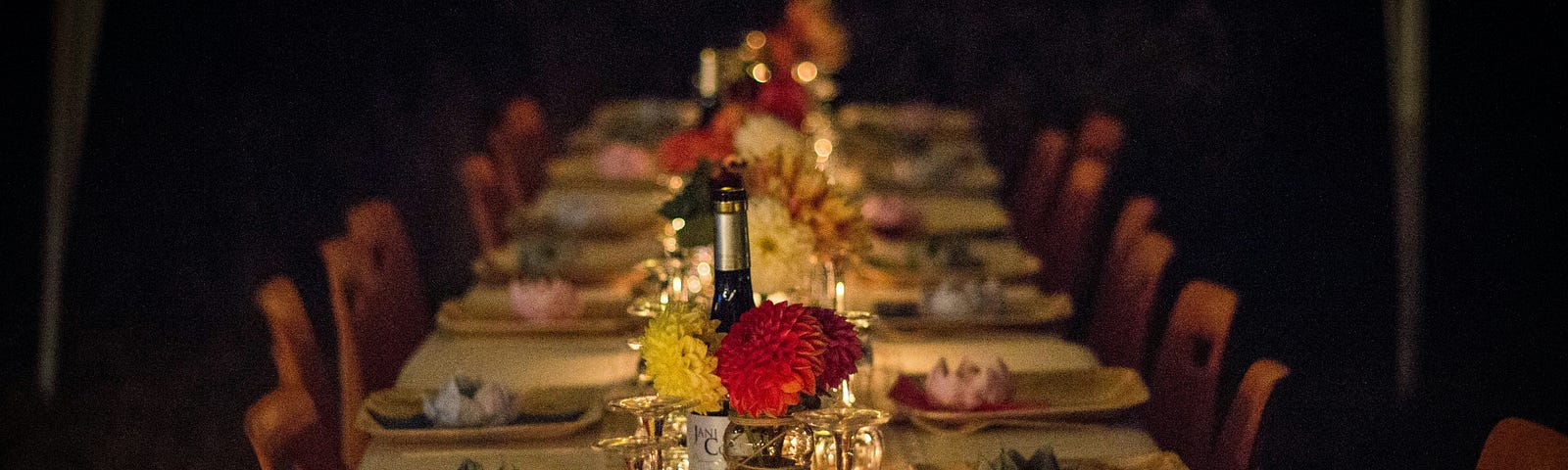 A lavish spread on a long table unoccupied, dim lit, with black background.