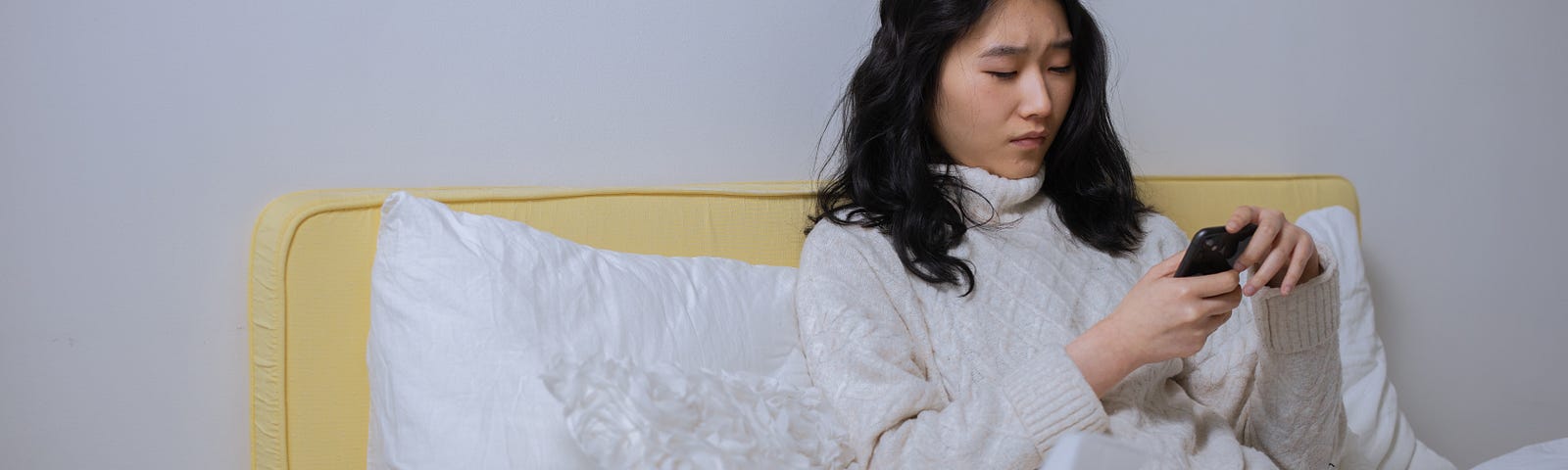 Woman in white sweatshirt sitting on bed.