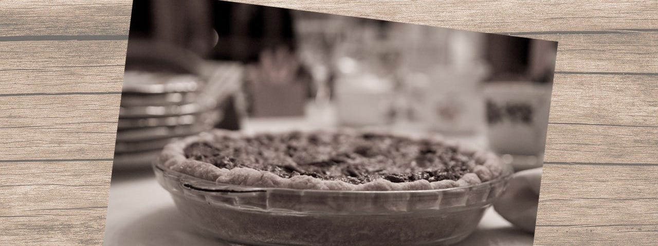 Black and white photo of a pecan pie in a glass baking dish on a kitchen counter against a woodgrain background