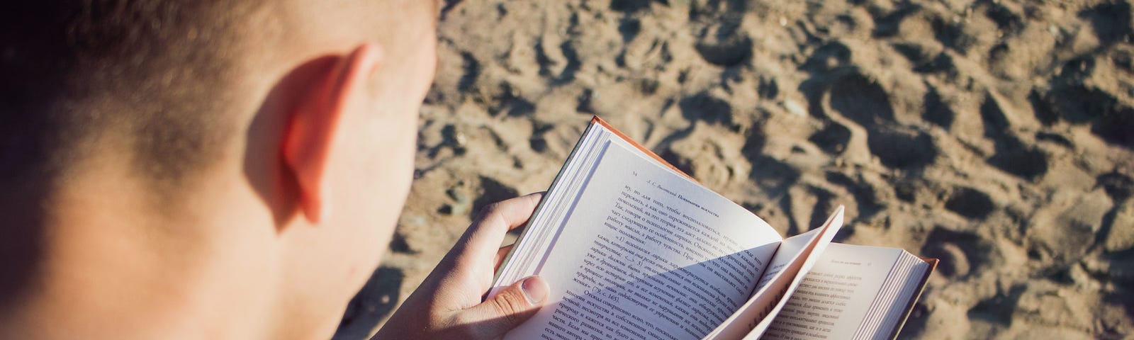 A man sits on the beach with an open book.