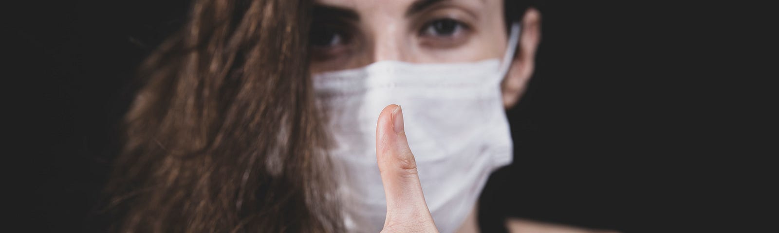 Person wearing a white mask and giving a thumbs up