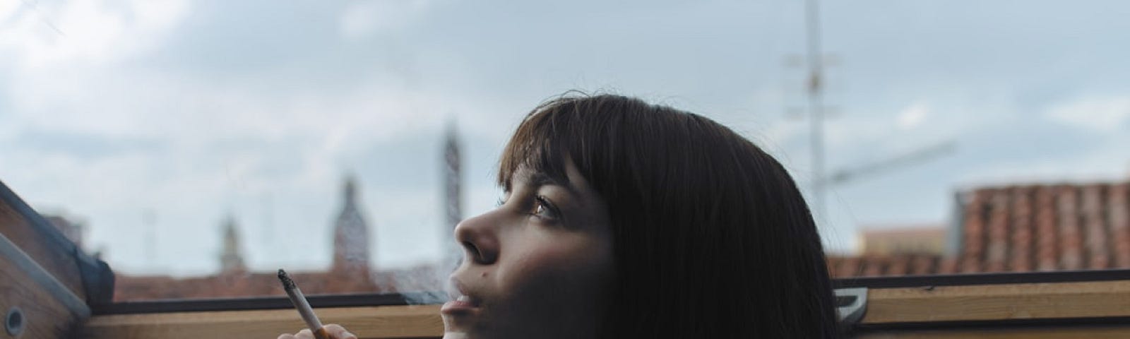 Young woman with dark hair smoking while looking thoughtfully up t the sky.