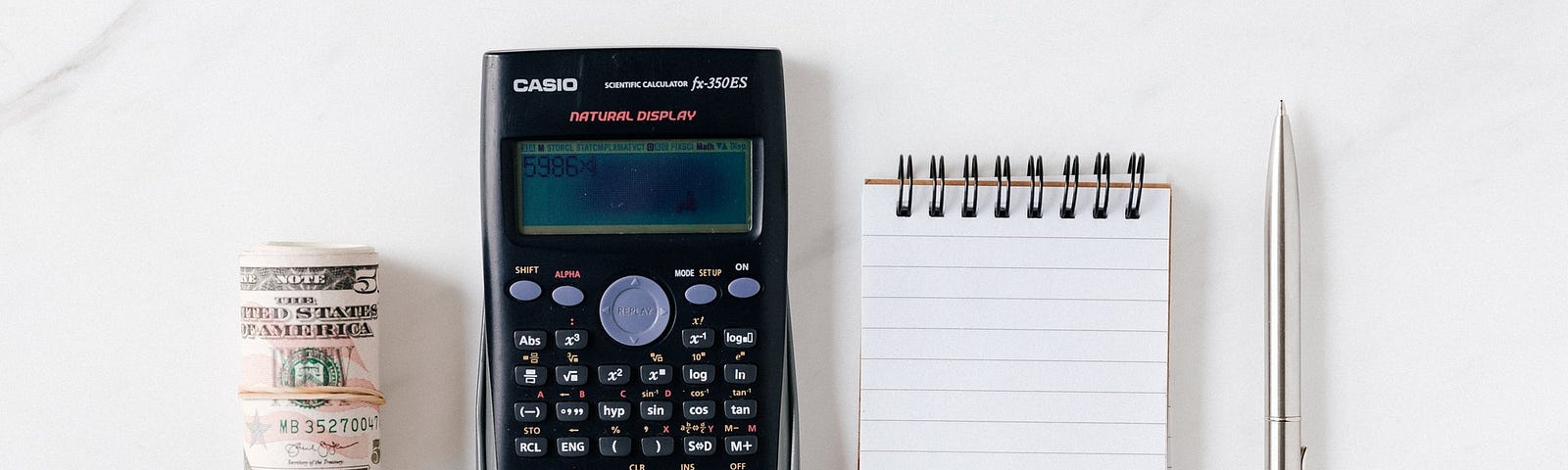 A roll of banknotes, a calculator, a notepad, and a pen