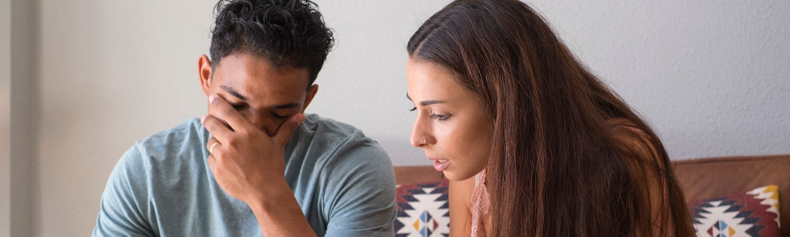 A man cradles his head in his hand while his partner jealousy rages over his phone.