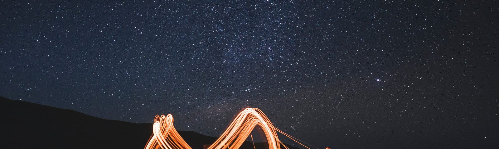 Man creating yellow infinity symbol with light standing in the darkness