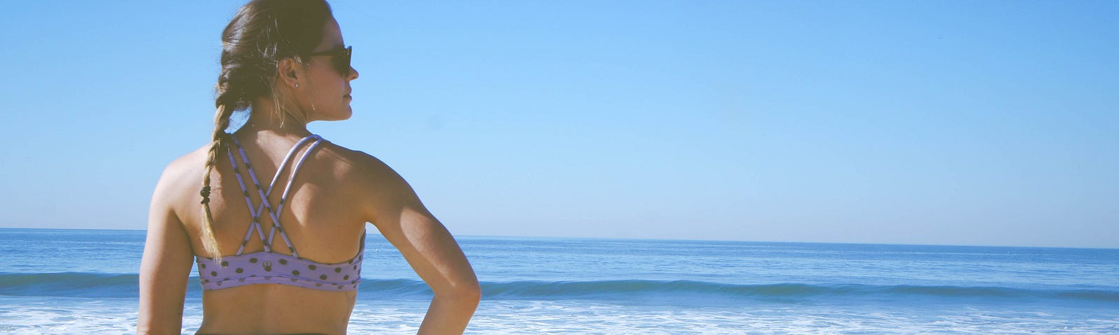 A woman stands on the beach in athletic wear staring out into the ocean with a renewed sense of confidence