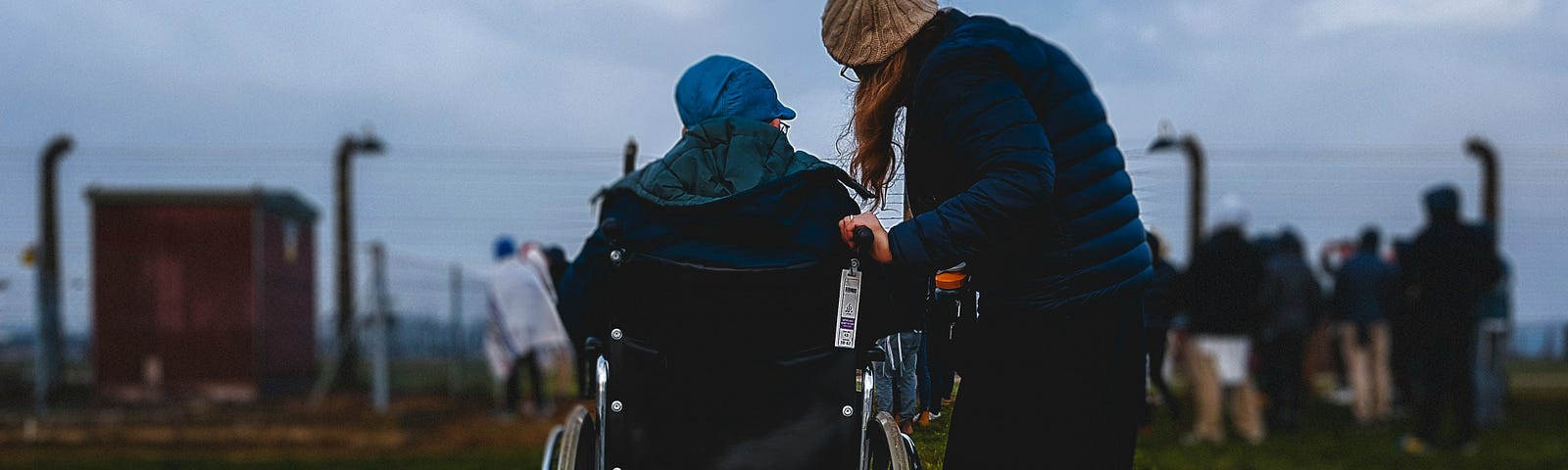 A Holocaust survivor in a wheelchair with a woman standing. They are watching Jewish youth playing in the death camp Auschwitz,