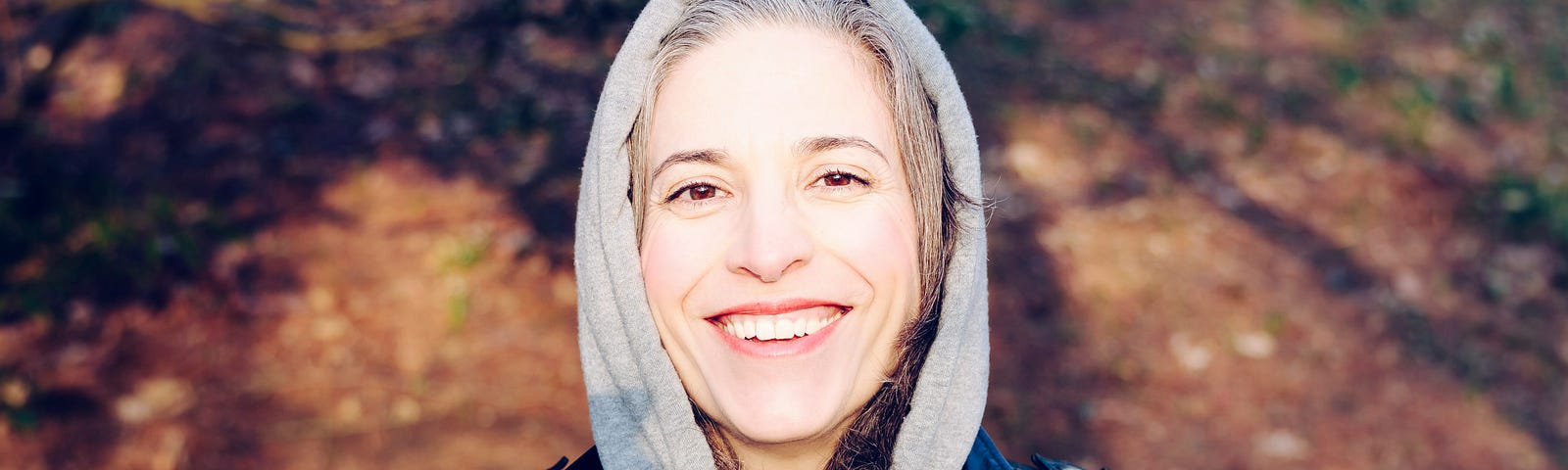 Beautiful older woman grinning at camera, wearing a gray hoodie and black leather jacket