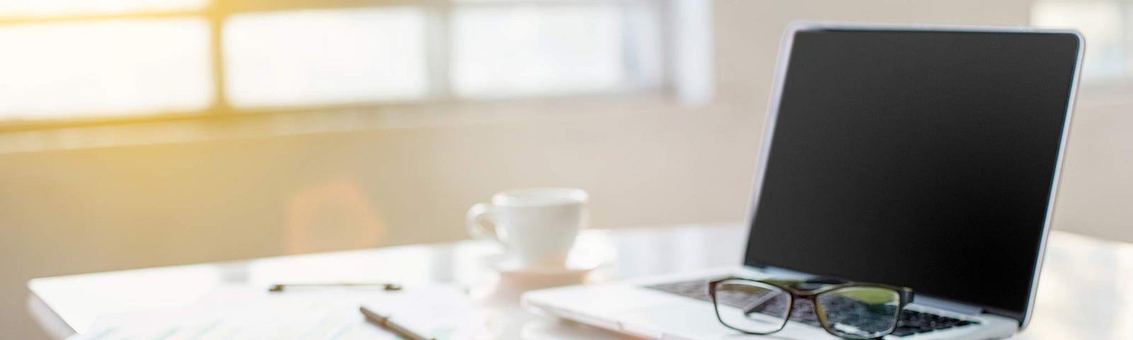 A desk with laptop, notepad, eyeglasses and iPad. No worker is present.