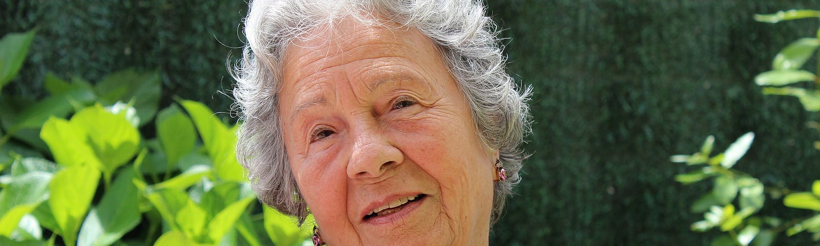 An older white haired woman sits on a chair, turns and looks at the camera.