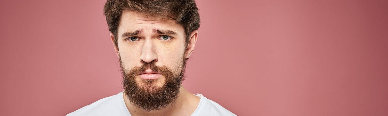 Gary, 25, with Hypersocial Disorder, Meets His Therapist — A Bearded Young Man with a Sad Expression on Pink Background