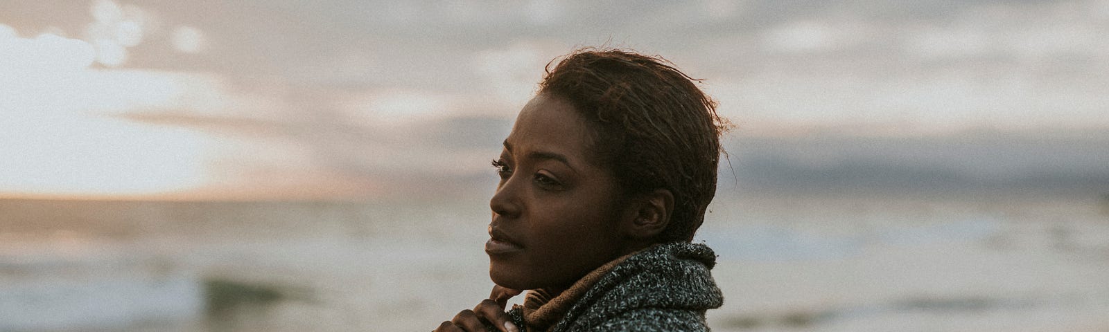 A woman gently touches her finger to her chin as she stares out across ocean.