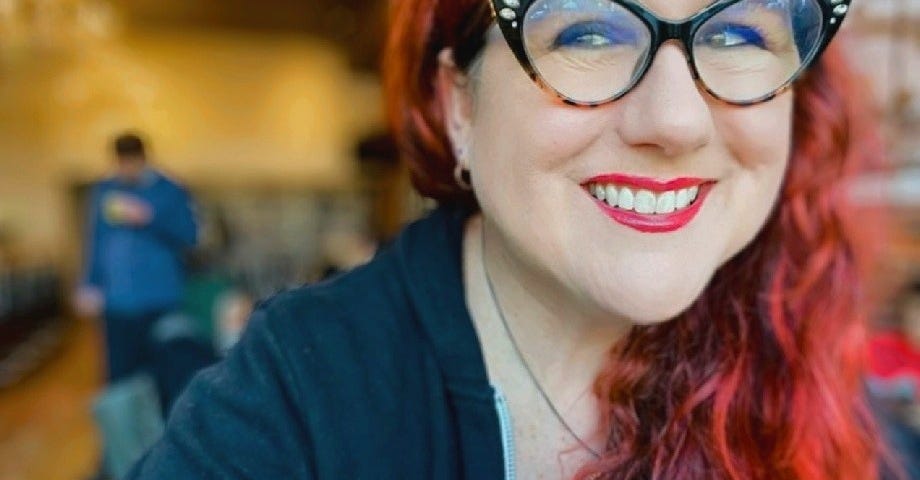 A redheaded woman with glasses, in a black sweater