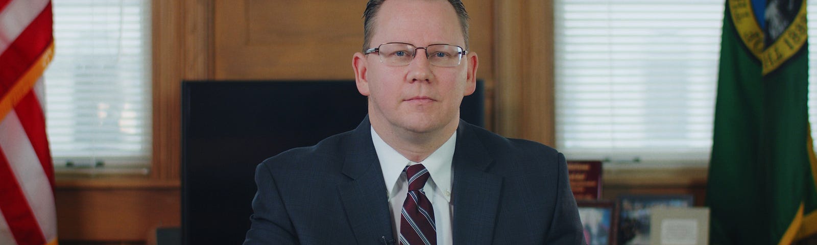 Superintendent Chris Reykdal sitting at his desk with his hands crossed in front of him.