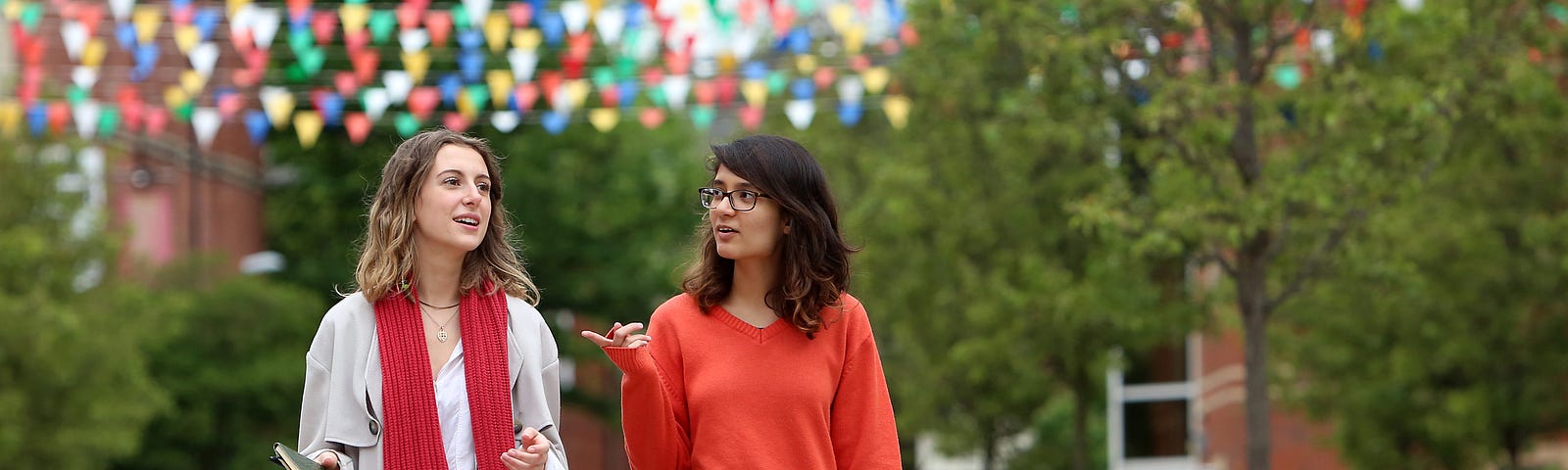 two students walking through campus, chatting to one another.