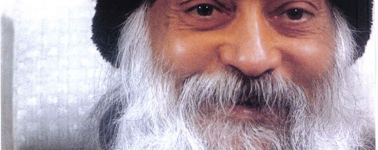 This is photo of a man in long white beard and moustache. His eyes sparkle and he’s smiling. His hands convey this expression of something meaningful that he is sharing with his audience. He’s dressed in a black hat and at tweed jacket.