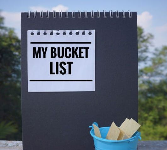 A sign reading “My Bucket List” with a bucket full of blank card against a leafy background.