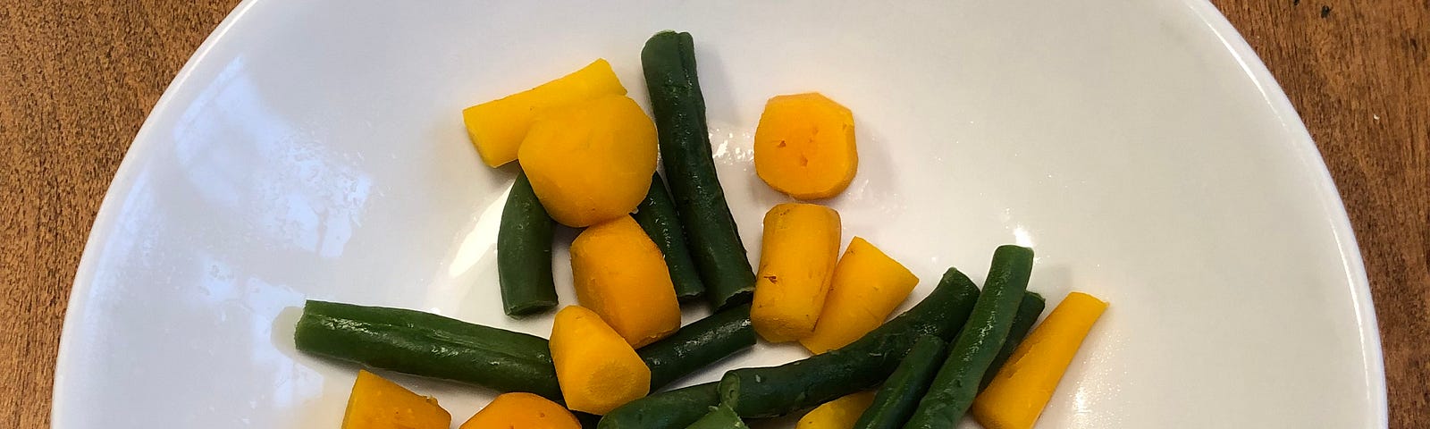 White plate with green beans and cut carrots on a wooden table