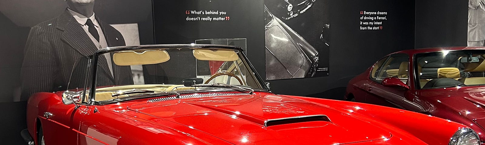 A red Ferrari GT250. Behind it on the wall a photograph of Enzo Ferrari with his quote, “What’s behind you doesn’t really matter”. The car is on display at Haynes Motor Museum, Sparkford, Yeovil, Somerset, England. Image: Roland Millward.