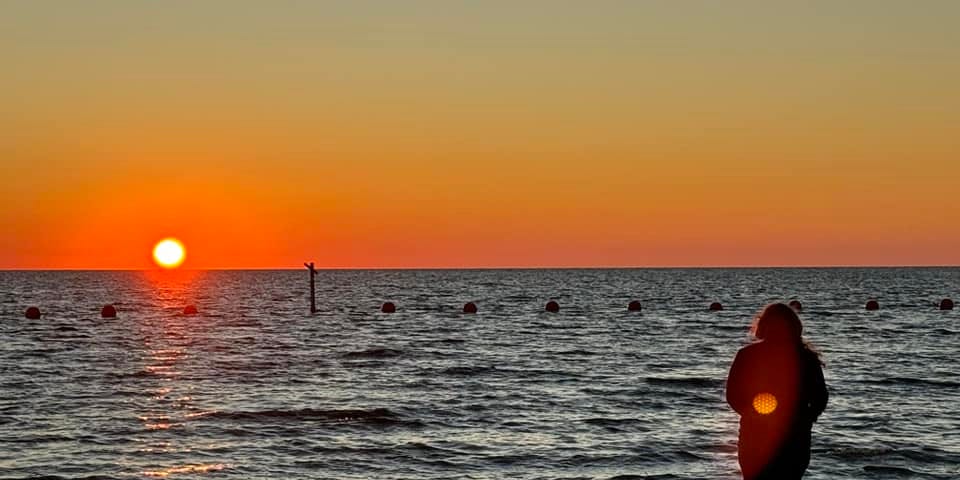 A woman stands at the beach and watches the sunset.