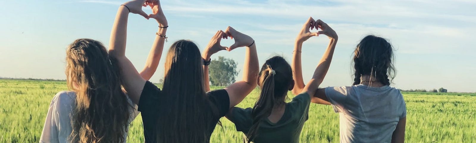 Teenage girls standing in a field and making heart shapes with their interlocked arms
