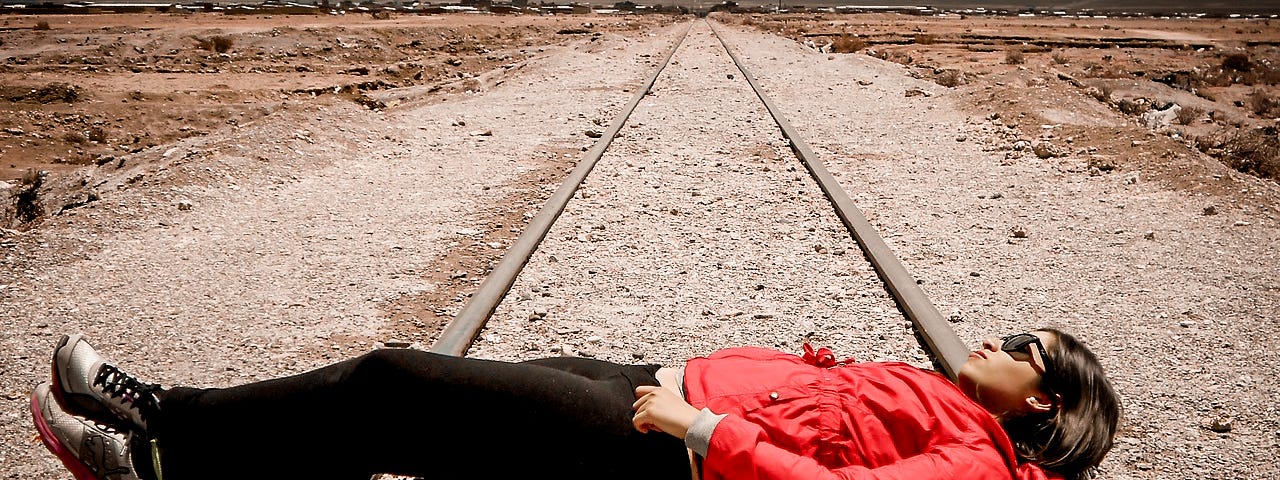 A woman in what appears to be a desert lying on railroad tracks.