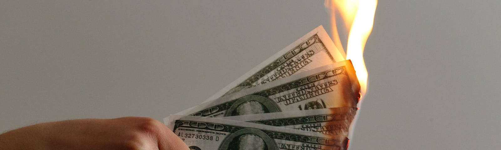 A hand holding hundred-dollar bills that are on fire