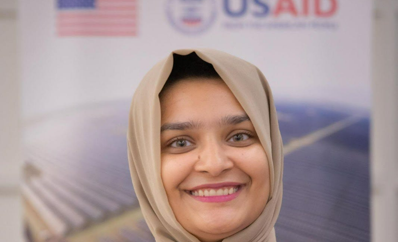 Closeup of a woman’s face in front of the USAID logo and American flag