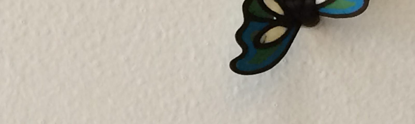 A blue green ceramic butterfly sits on the white washed wall.