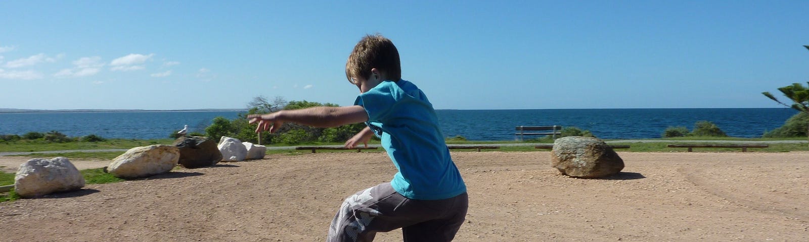 A young boy jumping from one large rock to another with the ocean background behind him