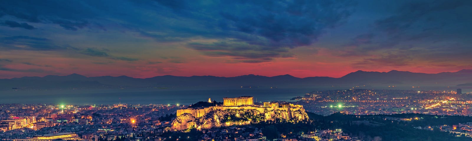 Image of Athens at night under Orange and deep Blue Sky. The city and the acropolis is lit up by lights