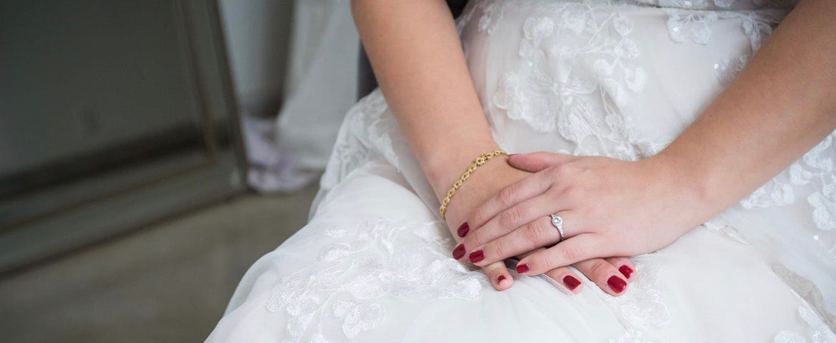 A bride’s hands are folded in her lap, engagement ring adorning her rouge painted fingers. Feels hopeful, expectant.