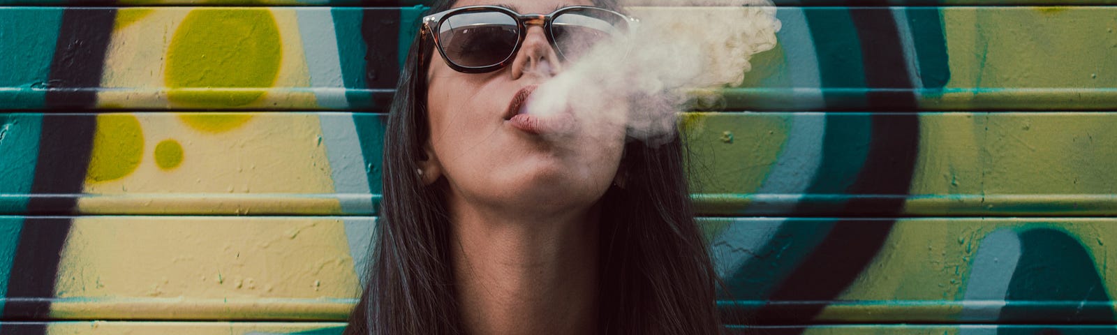 Woman exhaling smoke in front of a wall with graffiti