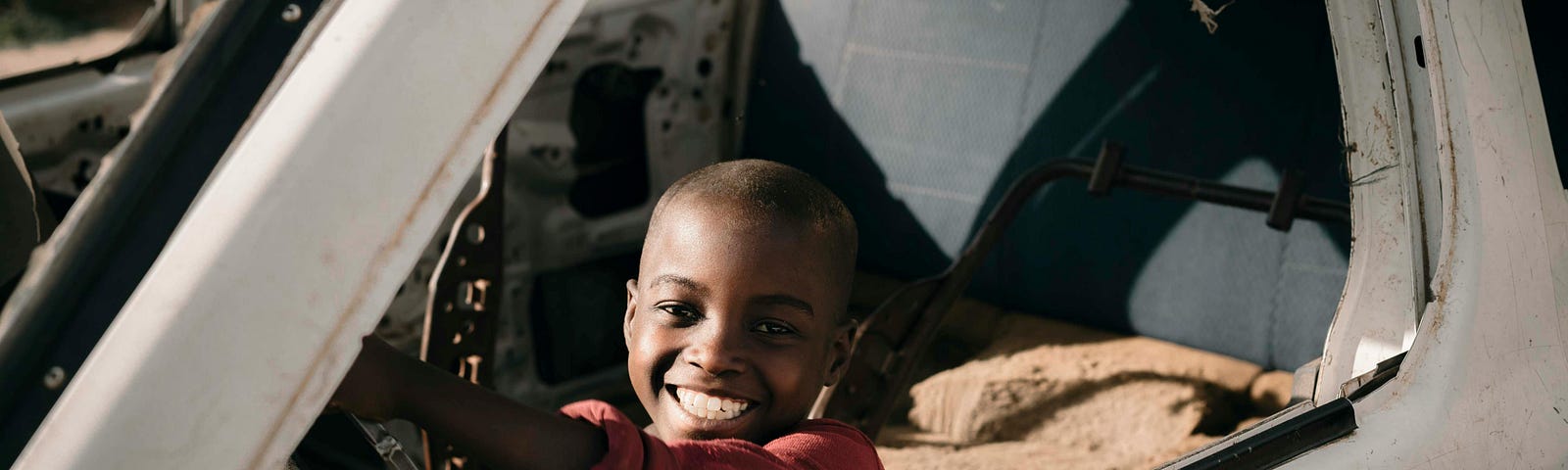 A small poor playing with a dilapidated car