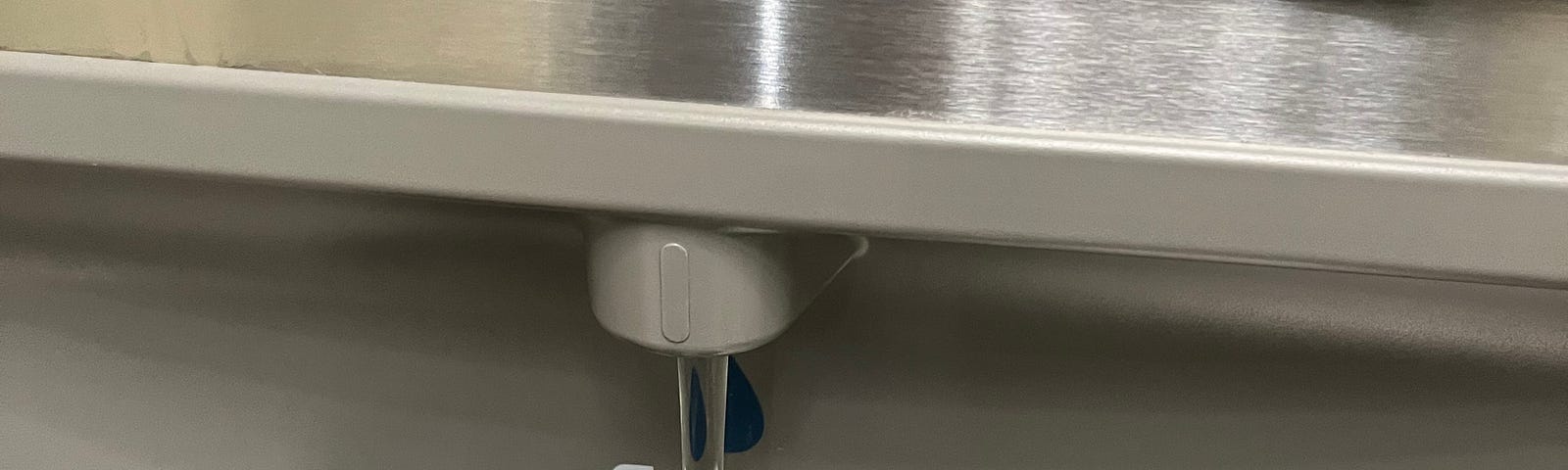 Photo of a hand holding a metal water bottle to refill at a water filling station at an airport. Alt text to demonstrate the importance of alt text.