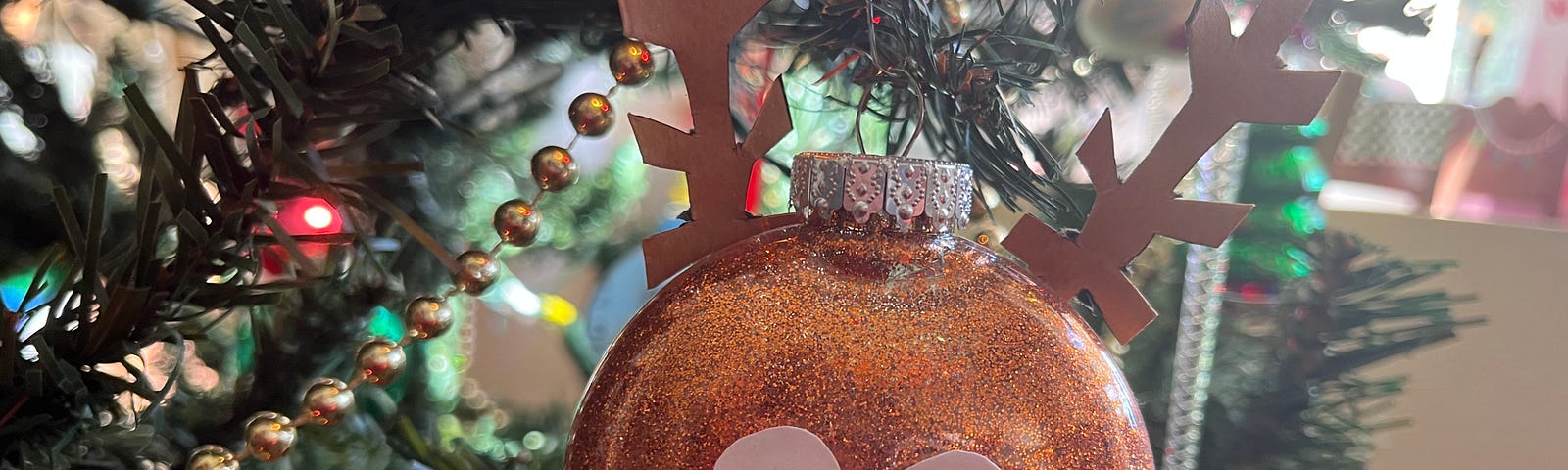 A handmade ornament of Rudolf the Red Nosed Reindeer hangs on a Christmas tree