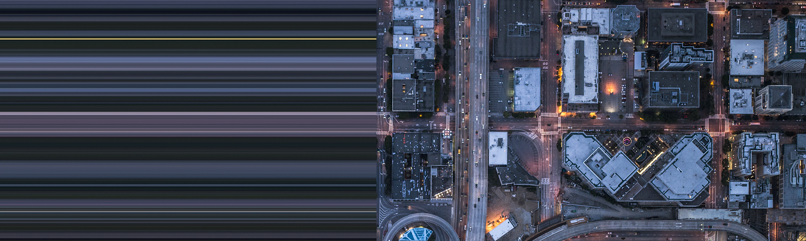 Aerial view of a city in the evening. The right side of the photo shows city blocks all lit up. The left side of the photo is stretched out and blurred.