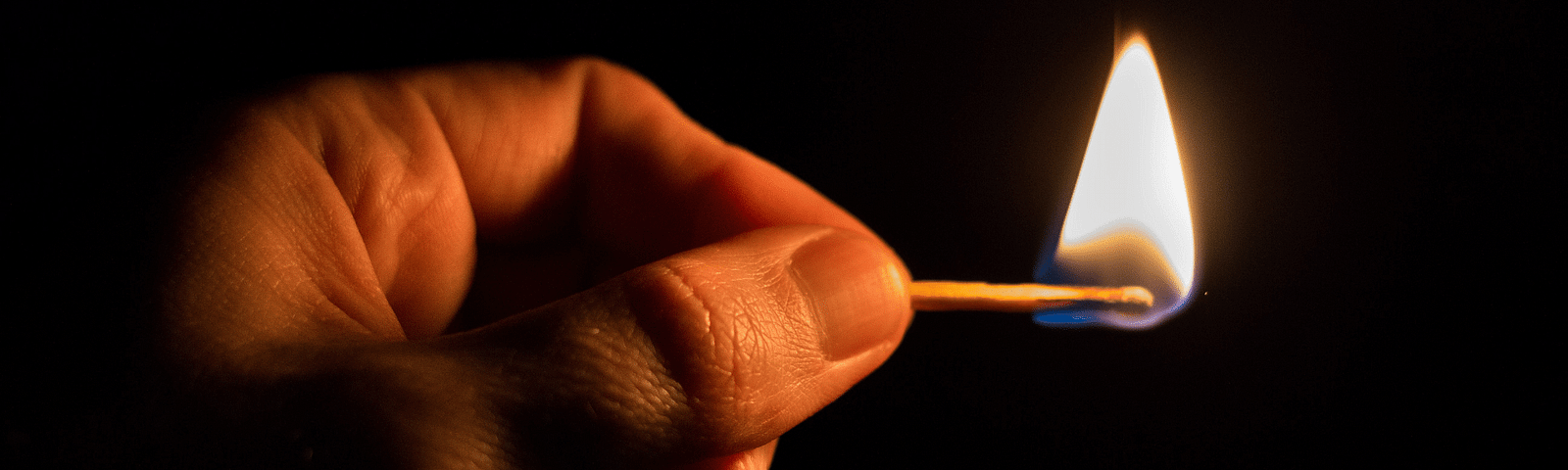 Image of a hand in the deep darkness, holding a flaming match.