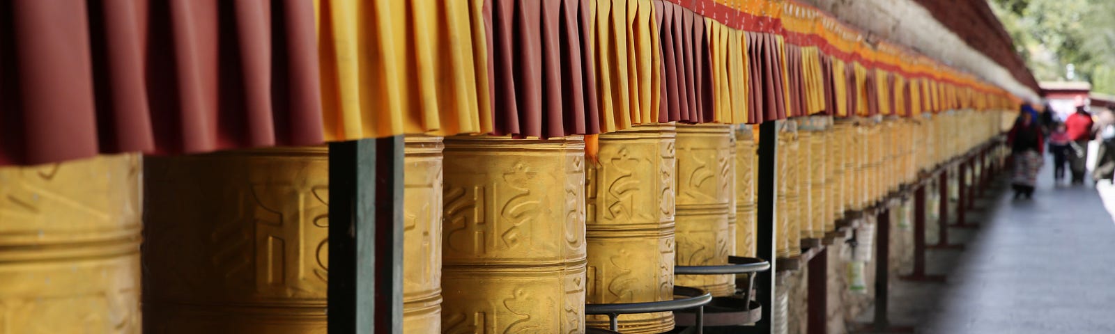 A colour image of a long line of Buddhist prayer wheels against a wall