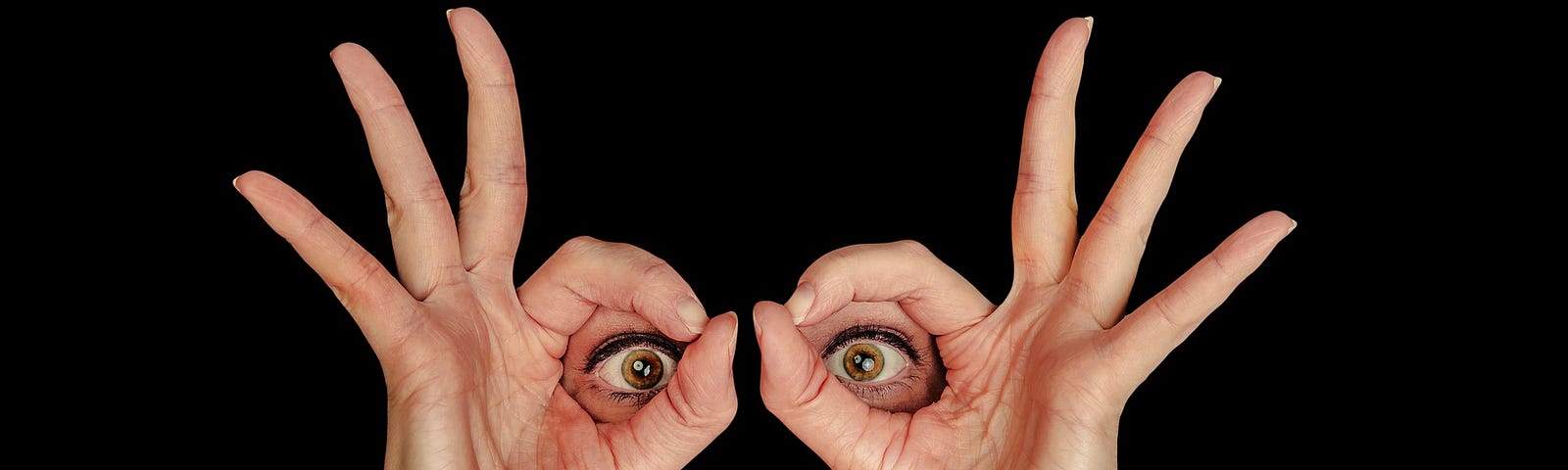 hands held to make glasses, framing eyes, with blackened background