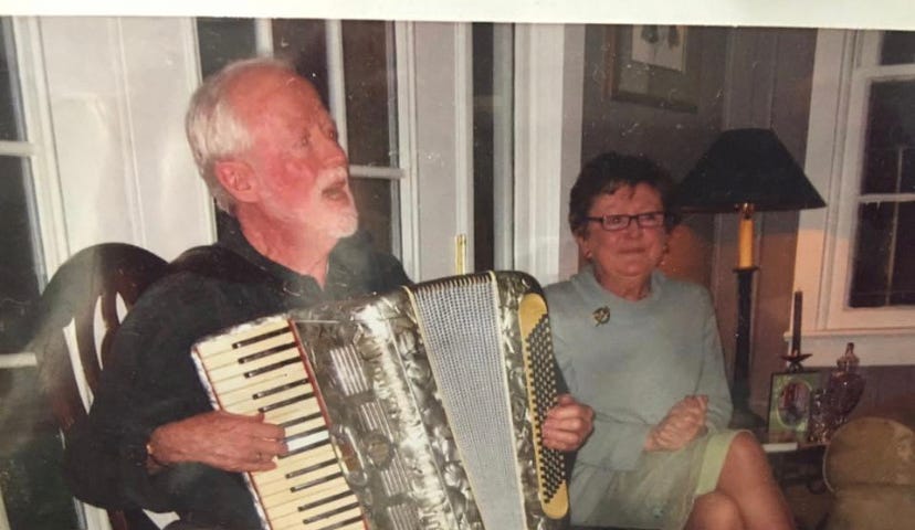 Man playing the accordion and singing with woman sitting beside him