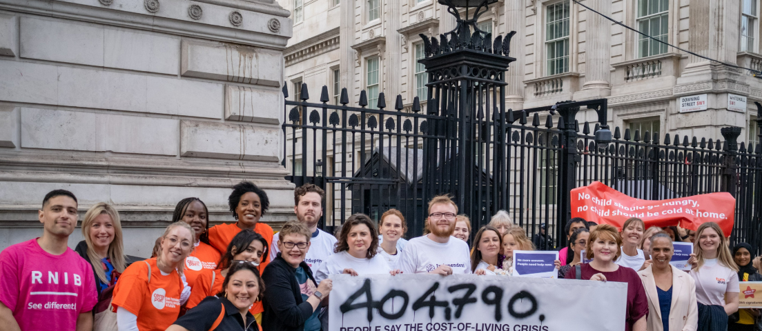 A group of people from different charities stand near Downing Street holding a large banner which reads that 404,790 people have signed a petition calling for benefits to be uprated in line with inflation.
