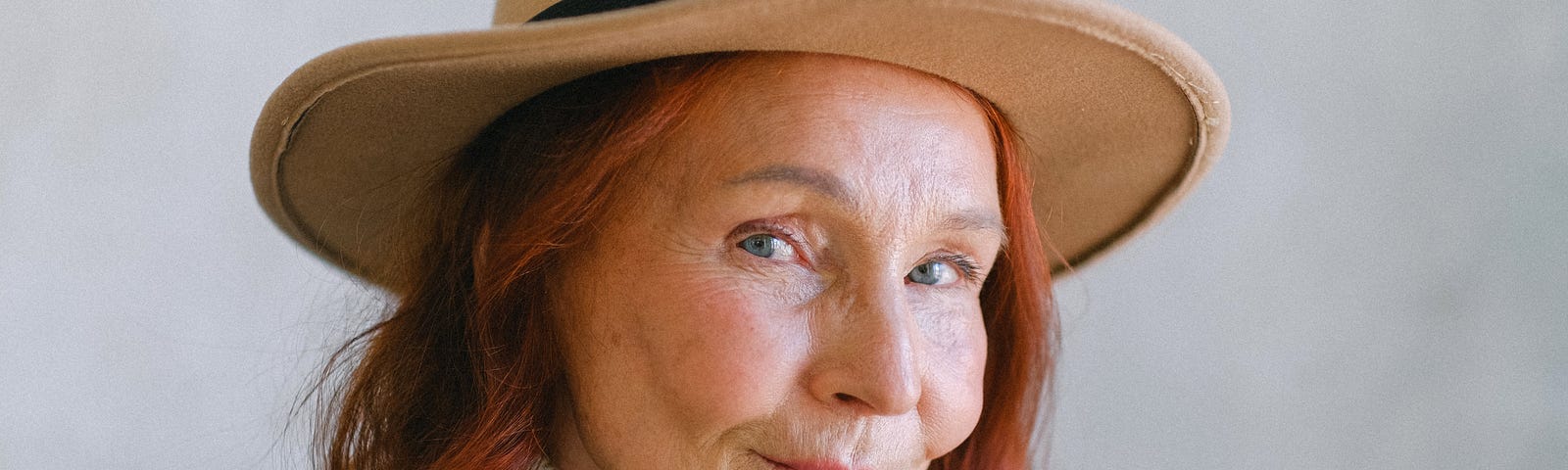 An older woman with red hair wears a straw hat and smiles