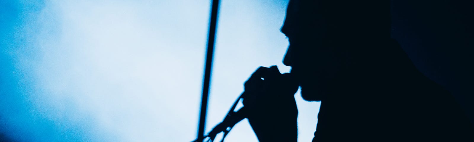 Silhouette of James Reid leaning into mic against blue stagelight and shadow.