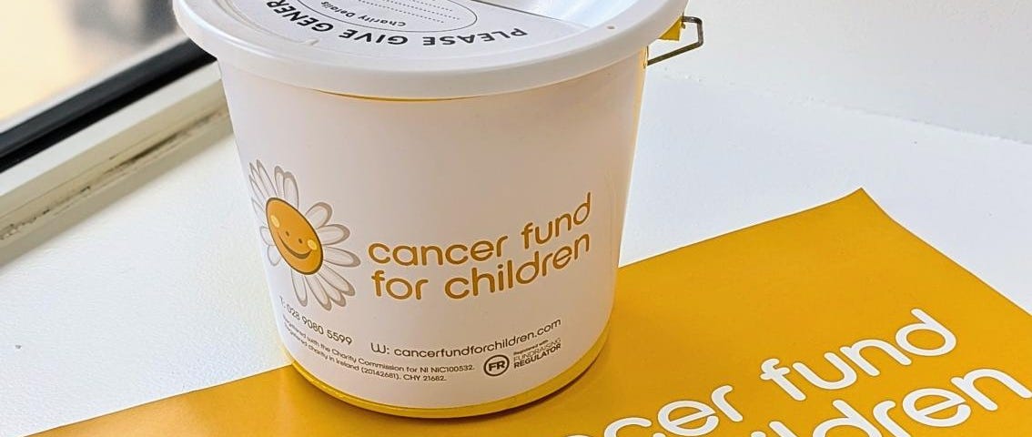 Image of a bucket and poster with a white and yellow Cancer Fund For Children logo