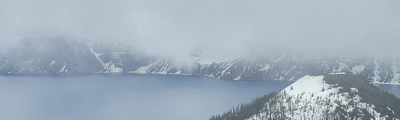 Dramatic photo of an island in the midst of crater lake. The other shoreline is heavily shrouded in fog.