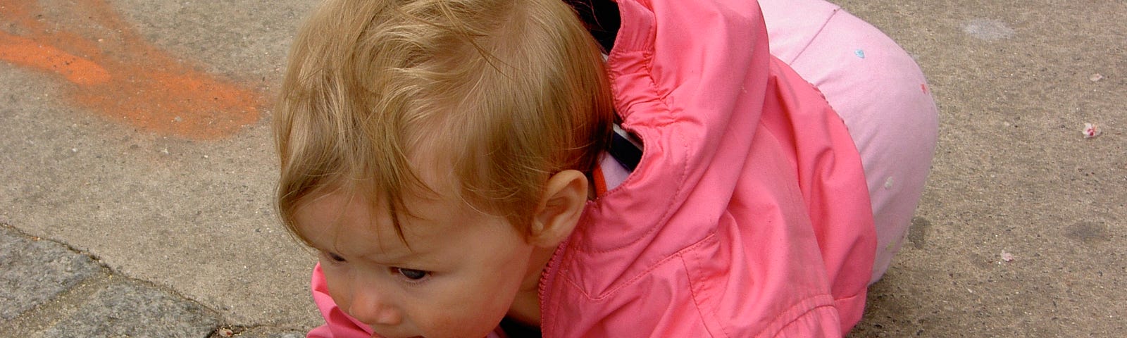 A baby clad in pink focuses on a pigeon off screen.