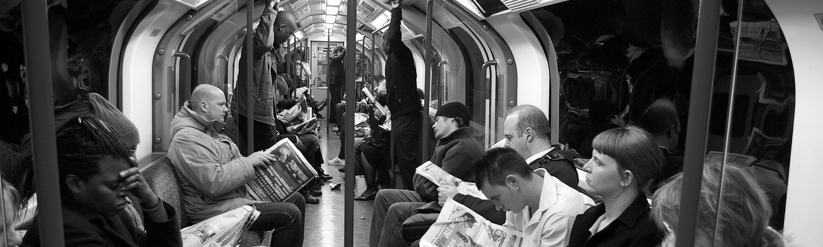 Black and white photo of commuters on the metro/subway reading newspapers. Routine mornings for workers on their way to work.